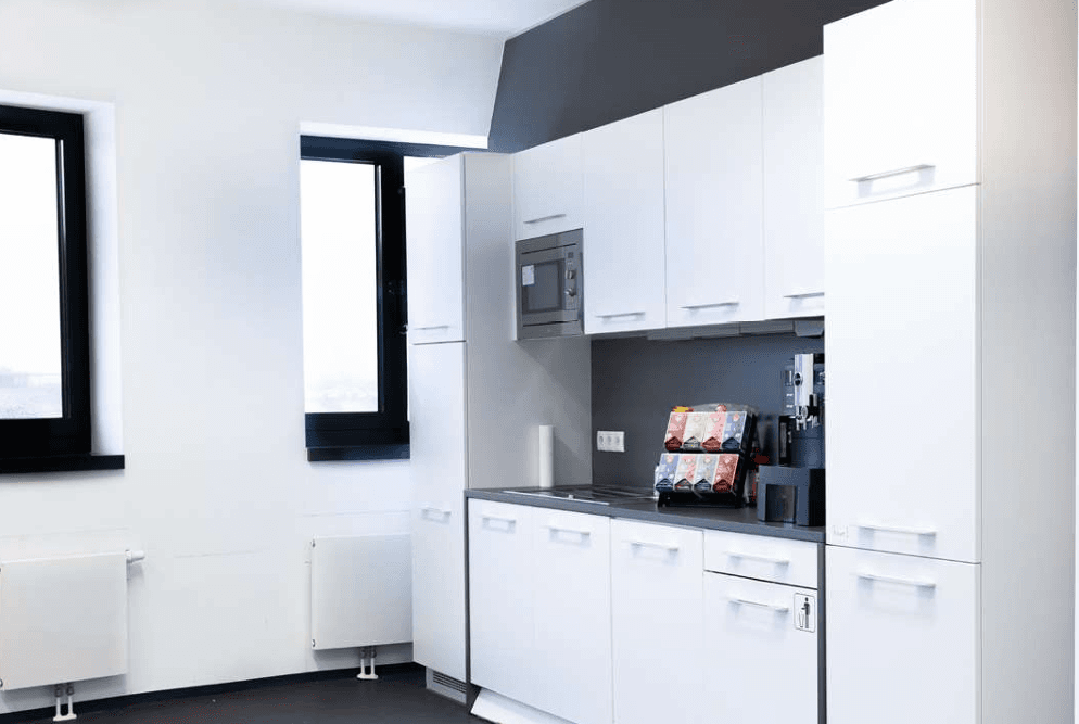 Funktionale Teeküche mit weißen Schränken, integrierter Mikrowelle und Kaffeemaschine, ideal für Büroräume.