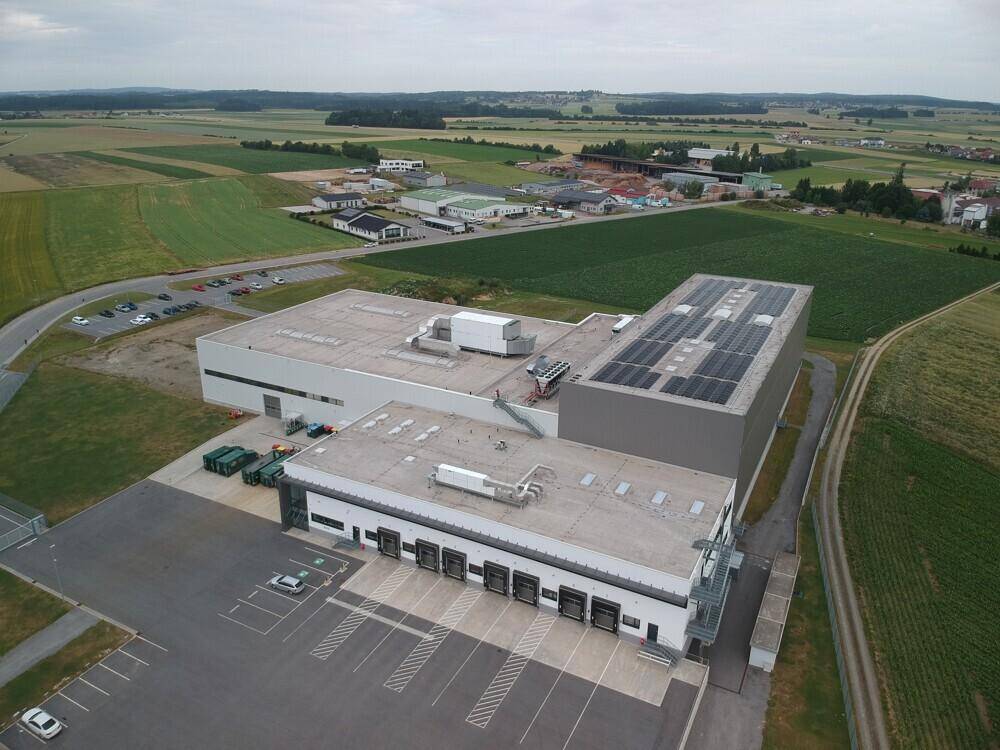 Luftaufnahme eines Industriegebäudes mit Photovoltaikanlage auf dem Dach und umliegender Landschaft.