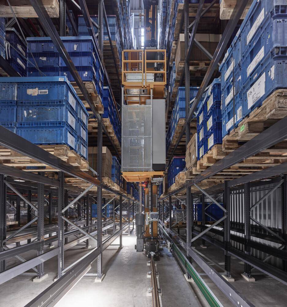 Innenansicht eines automatisierten Hochregallagers mit blauen Lagerbehältern und Fördertechnik.