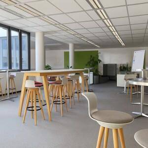 Offener Bereich mit hohen Tischen, Barhockern und grünen Akzentwänden in einem modernen Büro.