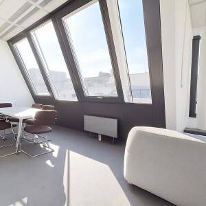 Sonniger Besprechungsraum mit schrägen Fenstern, einem Tisch und einer hellen Sitzbank.