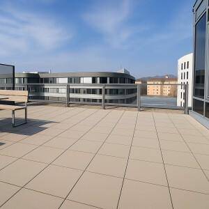 Große Dachterrasse mit Fliesenboden, Sitzbank und Blick auf umliegende Gebäude und die Landschaft.