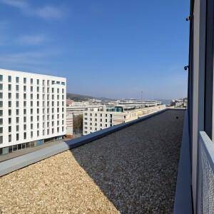 Weitläufiger Blick von einem Dach auf umliegende moderne Gebäude und die Stadtlandschaft.