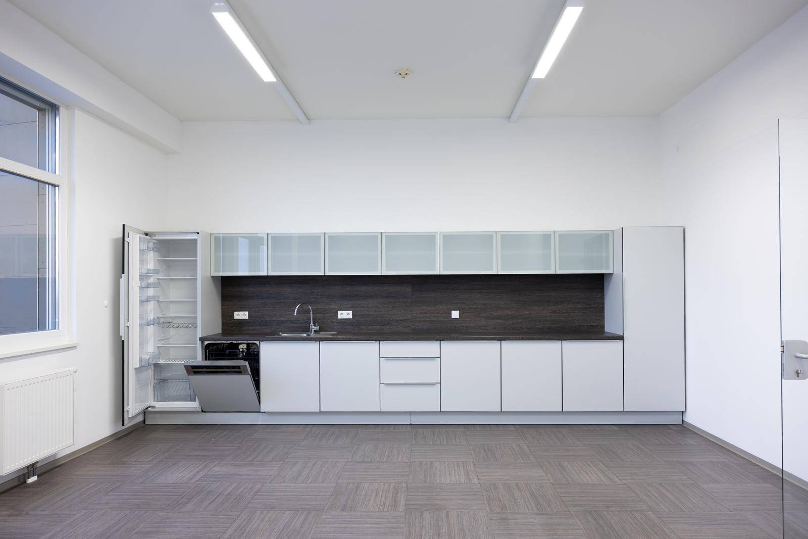 Moderne Einbauküche in einem Büro mit hellgrauen Schränken, Spülmaschine und Kühlschrank.