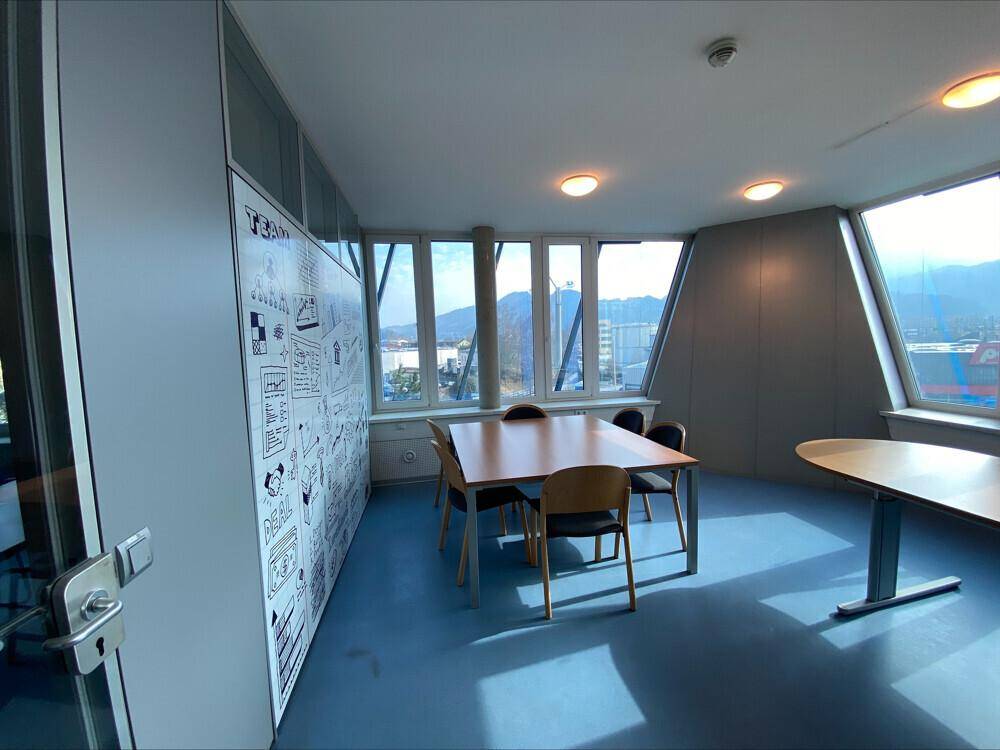 Konferenzraum mit moderner Wandgestaltung, großen Fenstern und Bergblick, bietet viel Tageslicht.