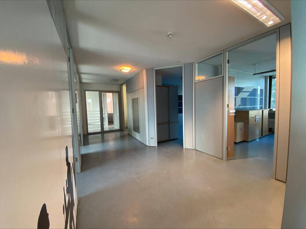 Geräumiger Flur mit hellen Wänden, Glastüren und Zugang zu verschiedenen Büroräumen.
