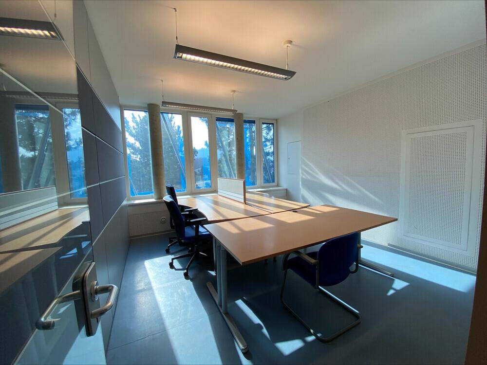 Büroraum mit zwei Arbeitsplätzen, großen Fenstern und viel Tageslicht, ideal für Teamarbeit.