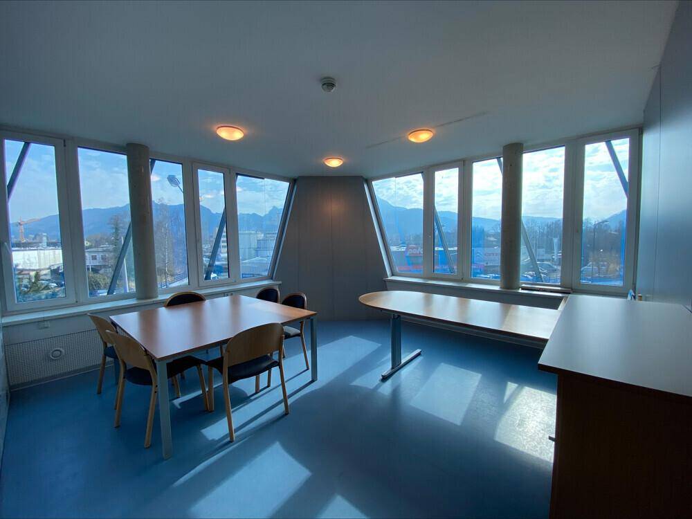 Heller Konferenzraum mit großen Fenstern, blauer Boden und Bergblick, ideal für Besprechungen.