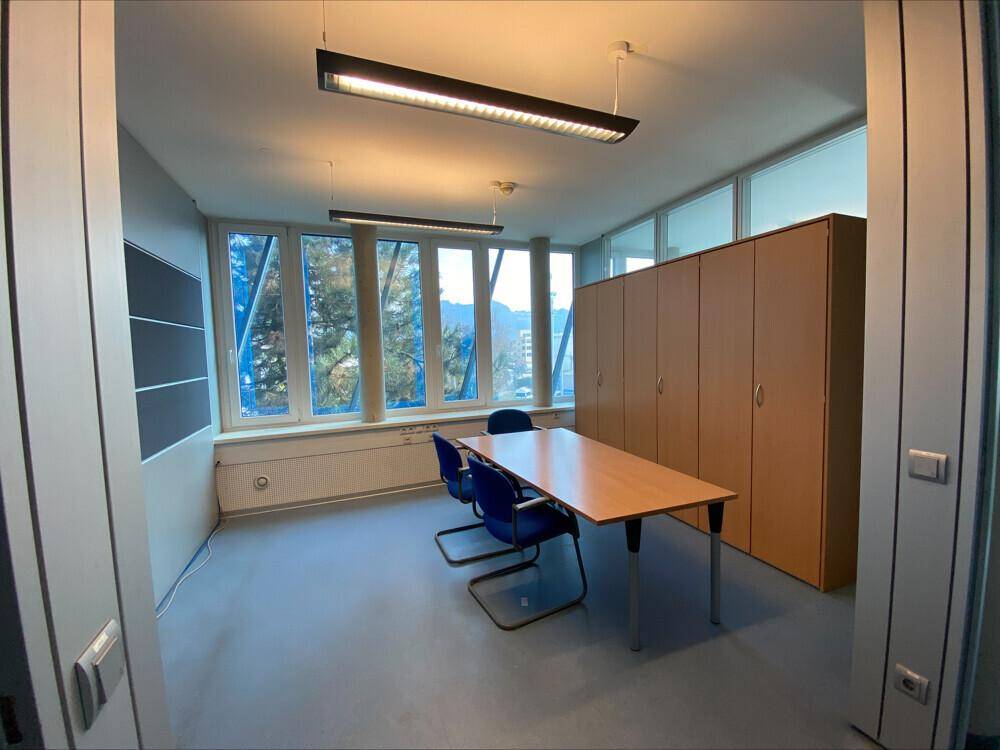 Büroraum mit Besprechungstisch, Schränken und Fenstern mit natürlichem Lichteinfall.