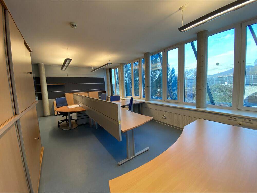 Büroraum mit mehreren Arbeitsplätzen, Trennwänden und Fenstern mit Ausblick.