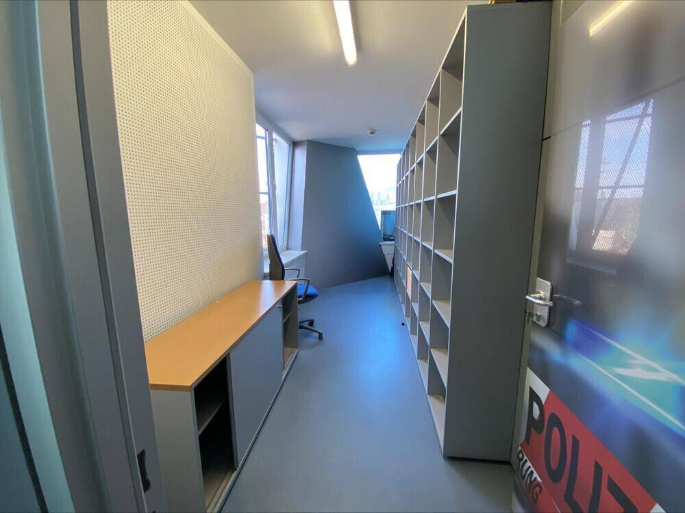 Schmaler Büroraum mit Regalen, Schreibtisch und Fenstern mit Ausblick, bietet Stauraum.