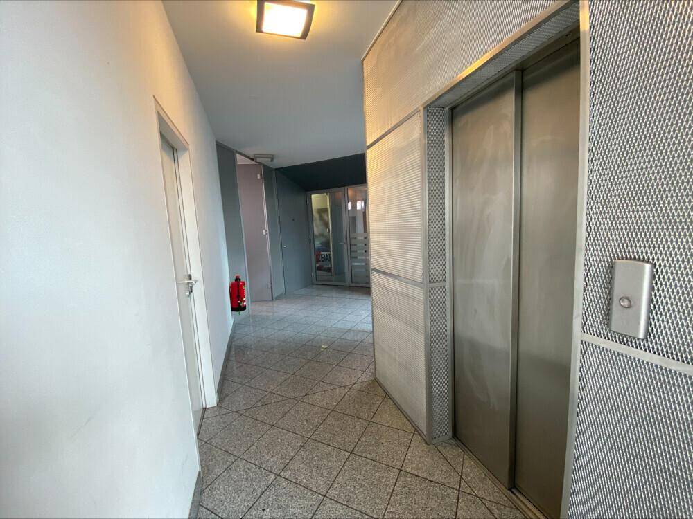 Flur mit Aufzug, gefliestem Boden und Zugang zu verschiedenen Bereichen im Gebäude.