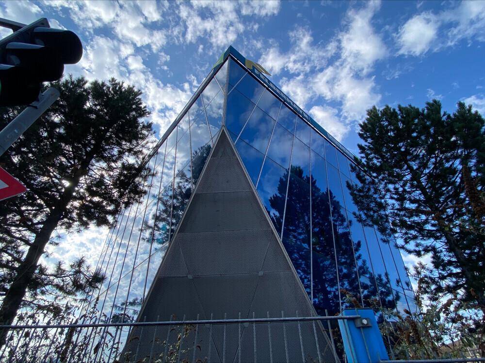 Moderne Gebäudefassade mit blauer Glasfront und markanter dreieckiger Struktur von unten gesehen.