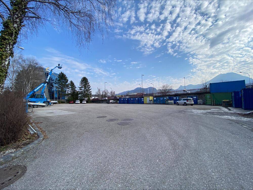 Großer Außenparkplatz mit Blick auf die Berge und umliegende Industriegebäude unter blauem Himmel.