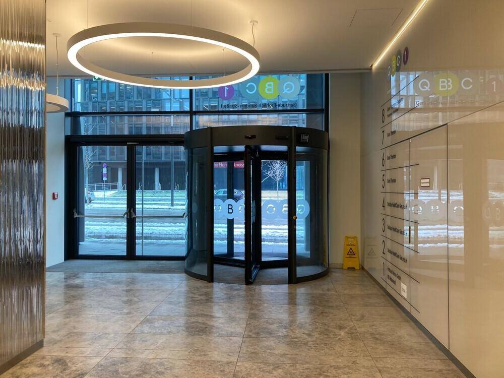 Moderner Eingangsbereich mit Drehtür, stilvoller Beleuchtung und elegantem Steinboden.