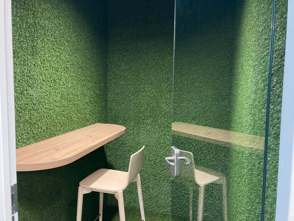 Einzigartiger Arbeitsbereich mit Wänden aus Kunstrasen, Holztheke und modernem Hocker.