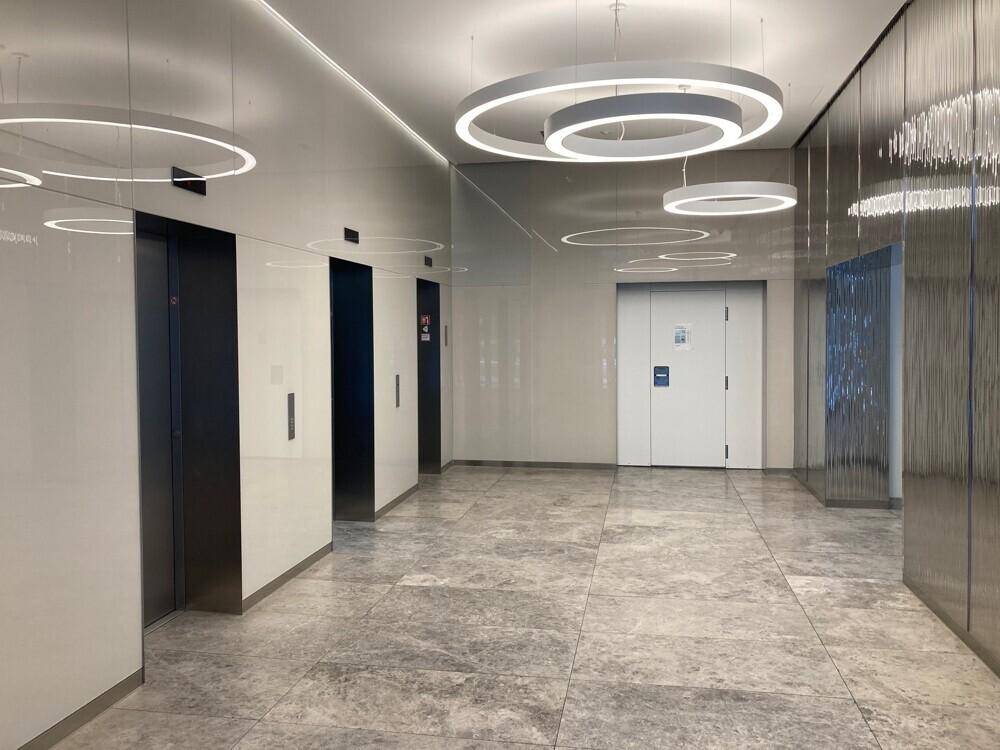 Eleganter Aufzugsbereich mit mehreren Aufzügen, modernen Ringlampen und hellem Steinboden.
