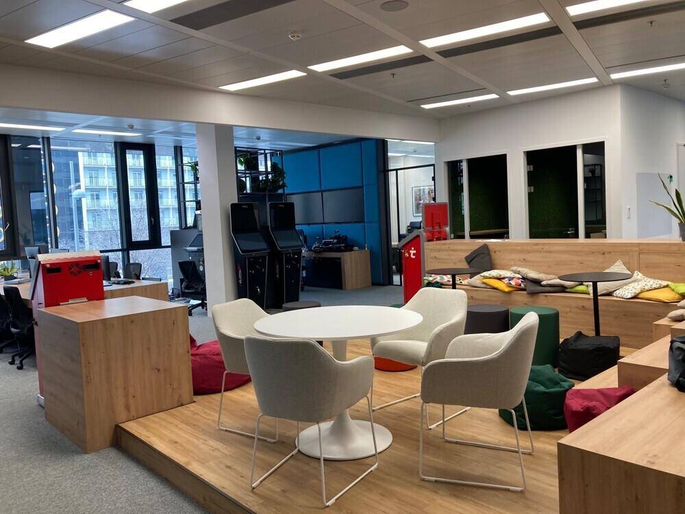 Offener Bürobereich mit verschiedenen Sitzgelegenheiten, erhöhter Plattform und modernen Möbeln.