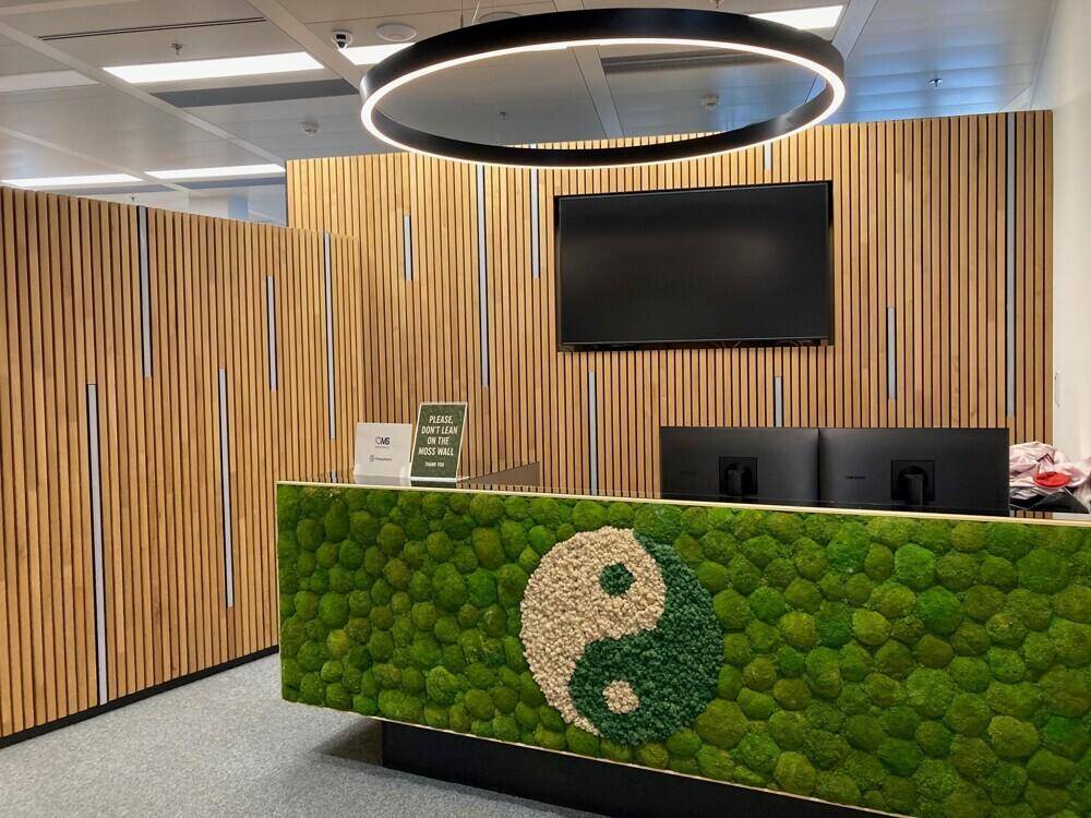 Detailansicht des Empfangstresens mit Mooswand, Yin-Yang-Symbol und Holzlamellenverkleidung.