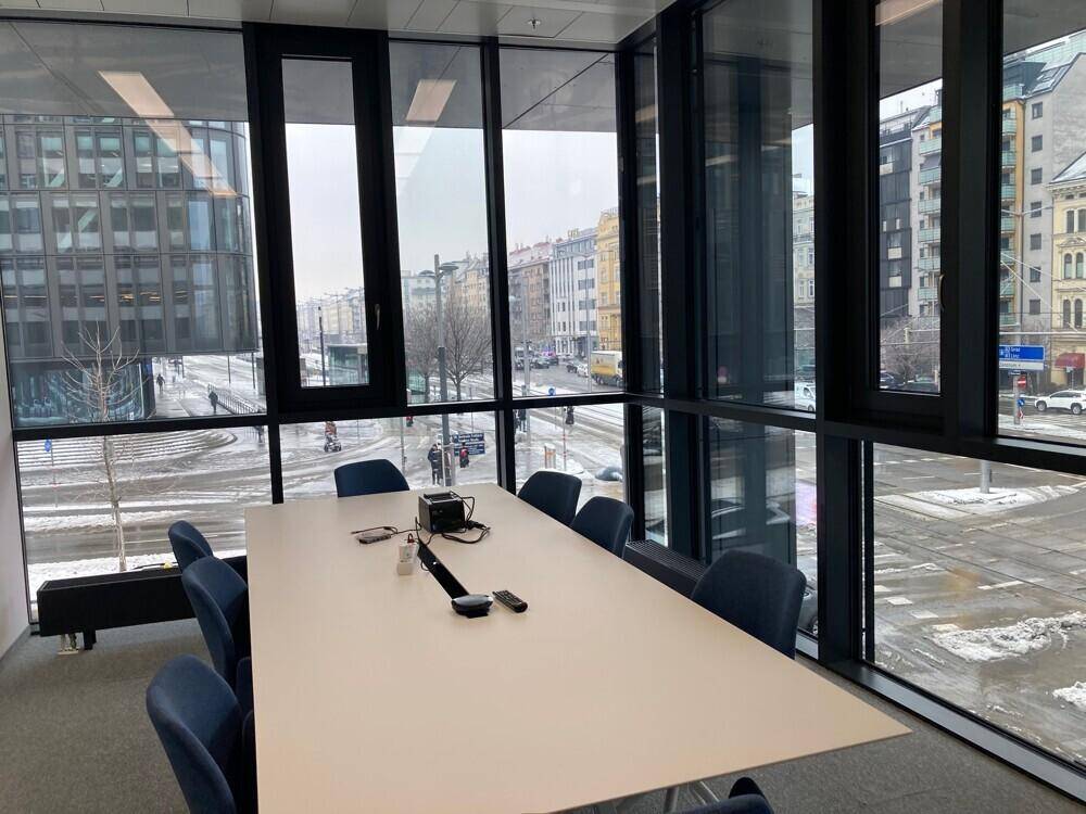 Konferenzraum mit großem Tisch, blauen Stühlen und raumhohen Fenstern mit Blick auf die verschneite Straße.