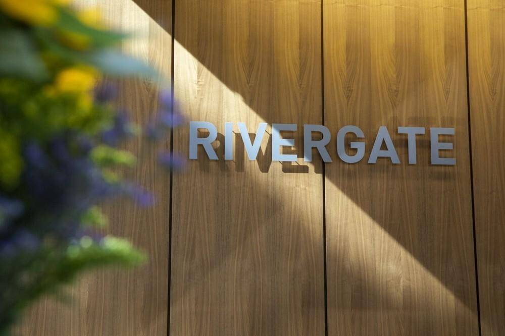Nahaufnahme des Schriftzugs "RIVERGATE" an einer Holzwand, mit unscharfen Blumen im Vordergrund.