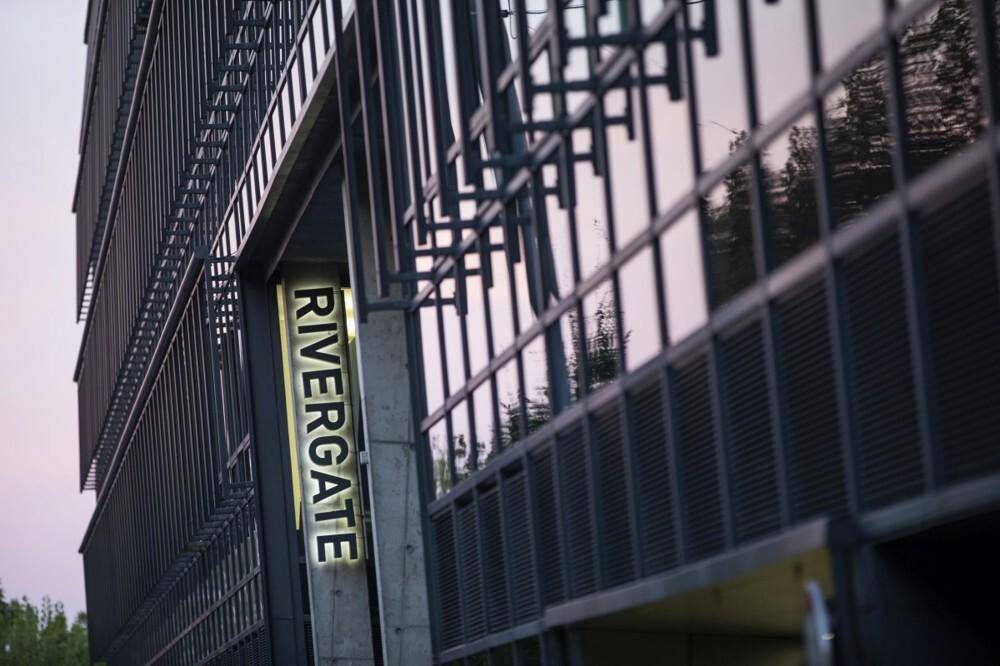 Außenansicht der Gebäudefassade mit einem vertikalen "RIVERGATE"-Schild und moderner Glas-Metall-Struktur.