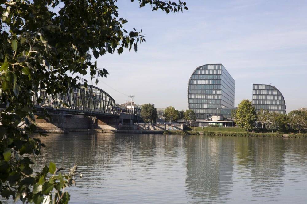 Modernes Bürogebäude mit geschwungener Glasfassade am Flussufer, im Hintergrund eine Brücke.