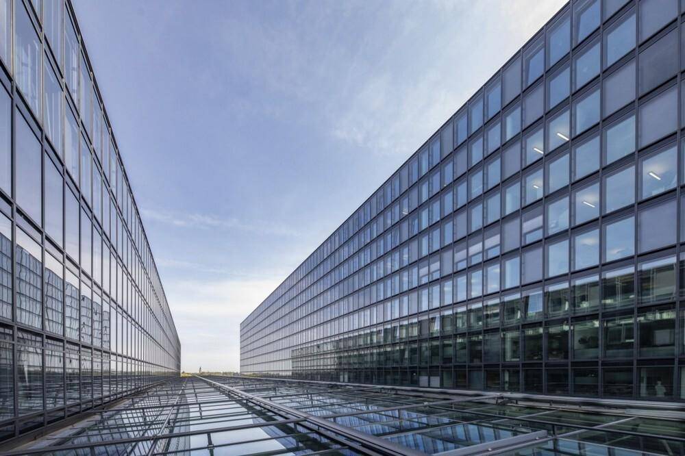 Perspektivische Ansicht von zwei modernen Gebäuden mit Glasfassaden unter blauem Himmel.