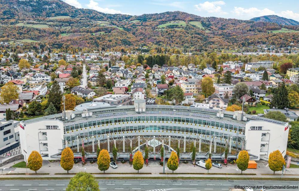 Weitläufige Luftaufnahme eines modernen Geschäftsgebäudes mit umliegender Stadtlandschaft und bewaldeten Bergen.