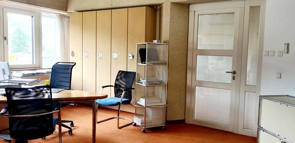 Funktionales Büro mit Holzschreibtisch, Bürostühlen und integrierten Aktenschränken entlang der Wand.