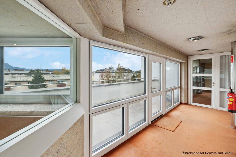 Langer Flur mit großen Fenstern, die einen weiten Blick auf die Stadt und die Berge bieten.