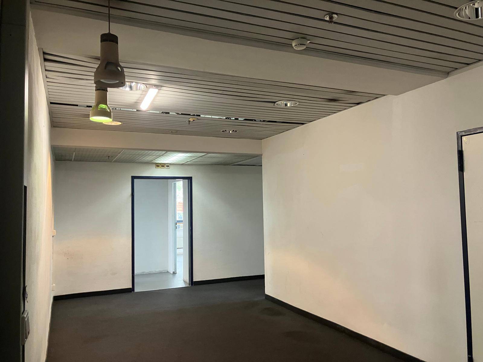 Langer, leerer Flur mit weißen Wänden, dunklem Teppichboden und einer abgehängten Decke.