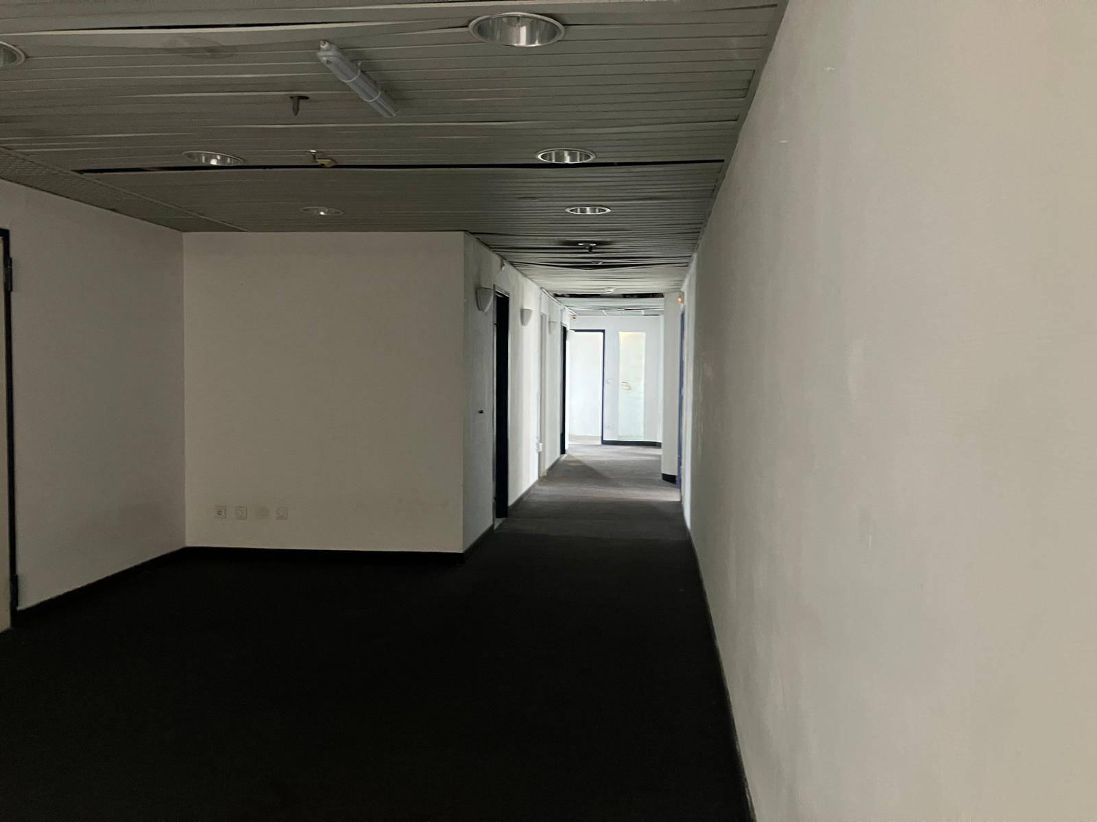 Langer Flur mit weißen Wänden und dunklem Teppichboden, der zu weiteren Räumen führt.