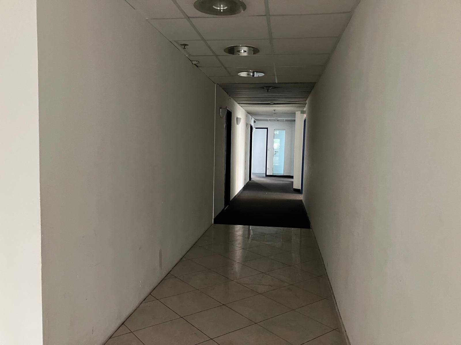 Langer, heller Flur mit weißen Wänden, gefliestem Boden und Deckenbeleuchtung.