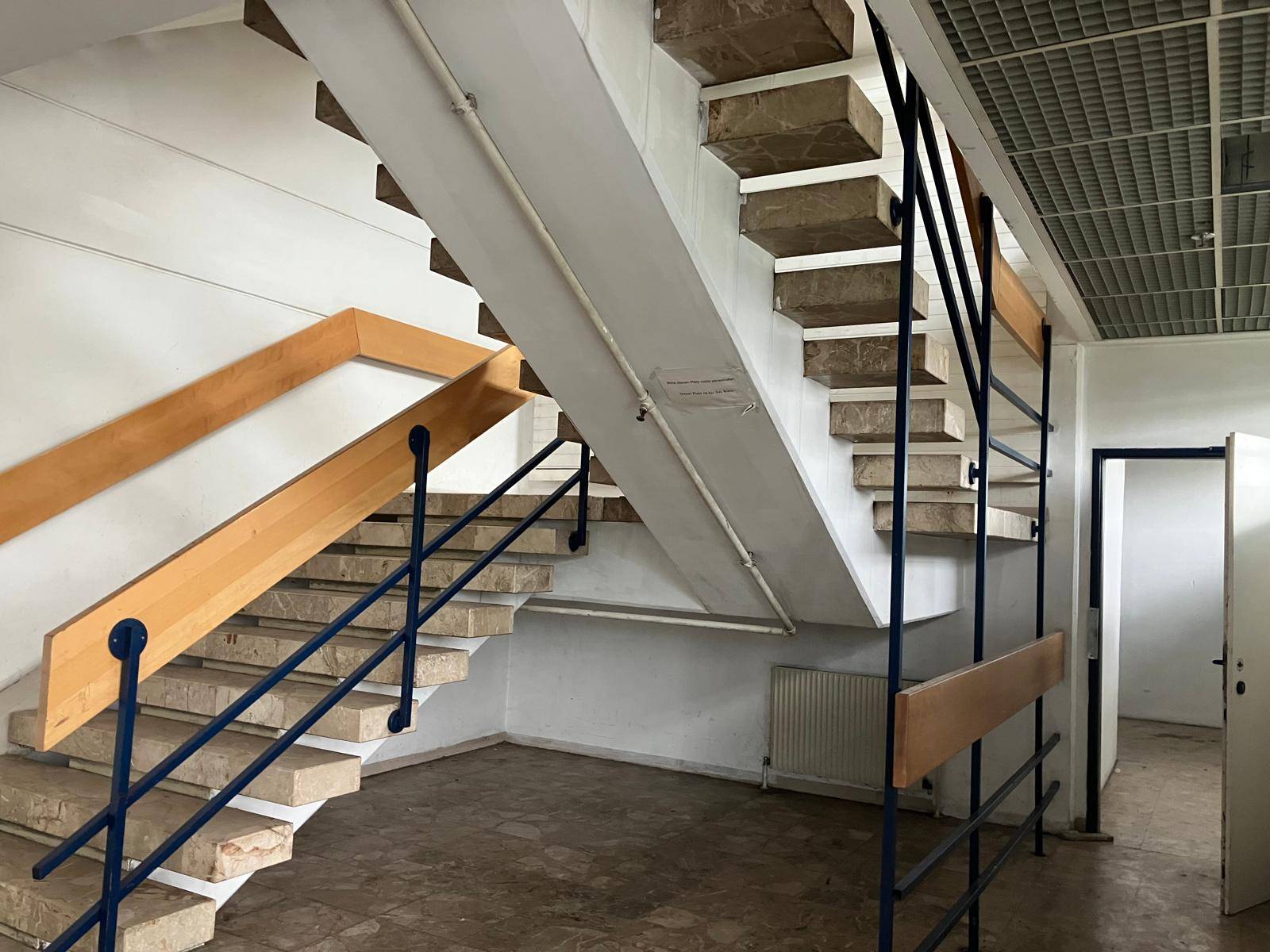 Geräumiges Treppenhaus mit Steinstufen, Holzhandläufen und Metallgeländern, führt zu den oberen Etagen.