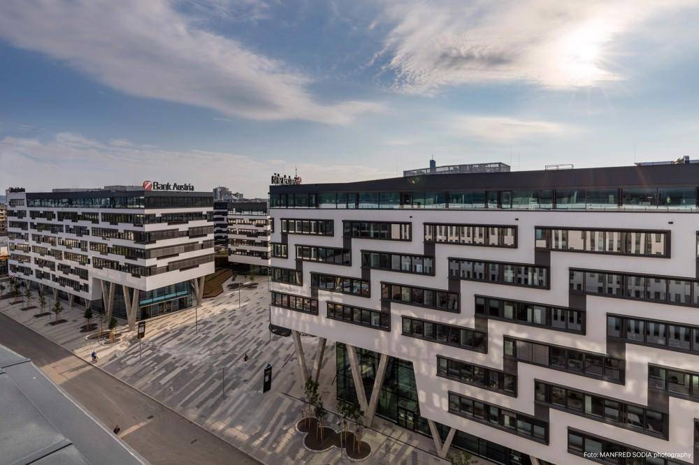 Weitläufige Ansicht moderner Bürokomplexe mit markanten Fassaden und einem belebten Vorplatz.