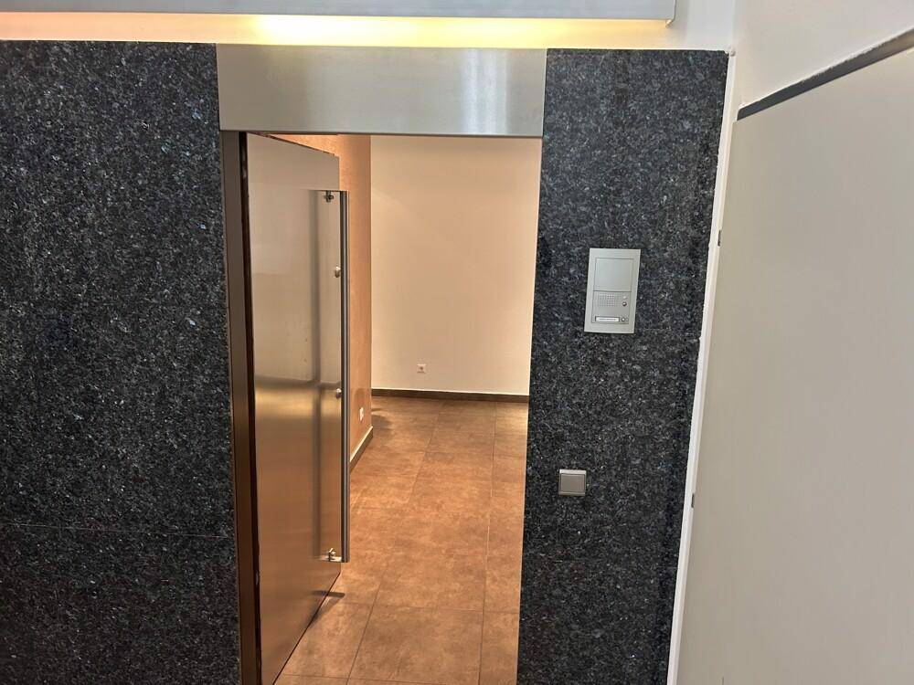 Moderner Eingangsbereich mit dunkler Granitverkleidung und einer eleganten Metalltür, die in den Flur führt.