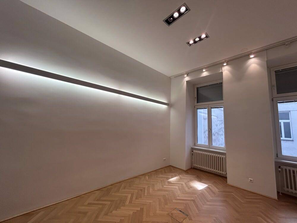 Heller Raum mit elegantem Fischgrätparkett, modernen Deckenleuchten und großen Fenstern für viel Tageslicht.