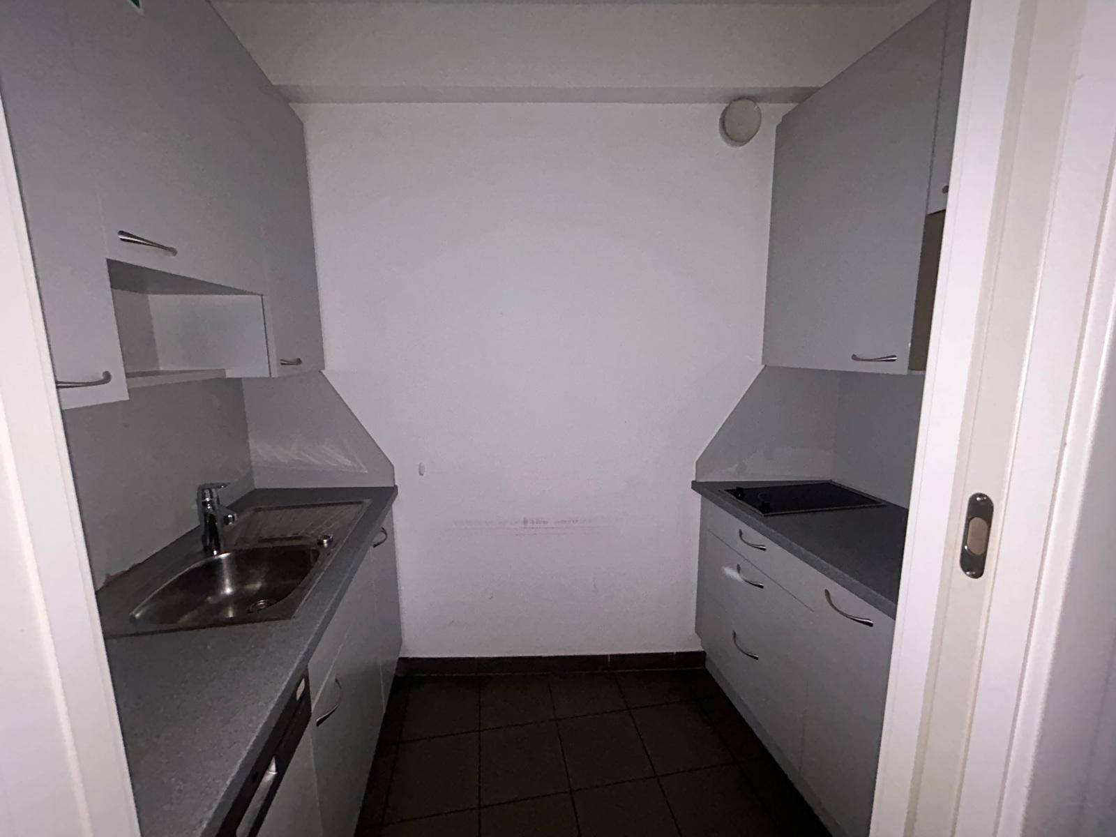 Kleine, funktionale Küchenzeile mit weißen Schränken, dunklen Fliesen und Dunstabzugshaube.
