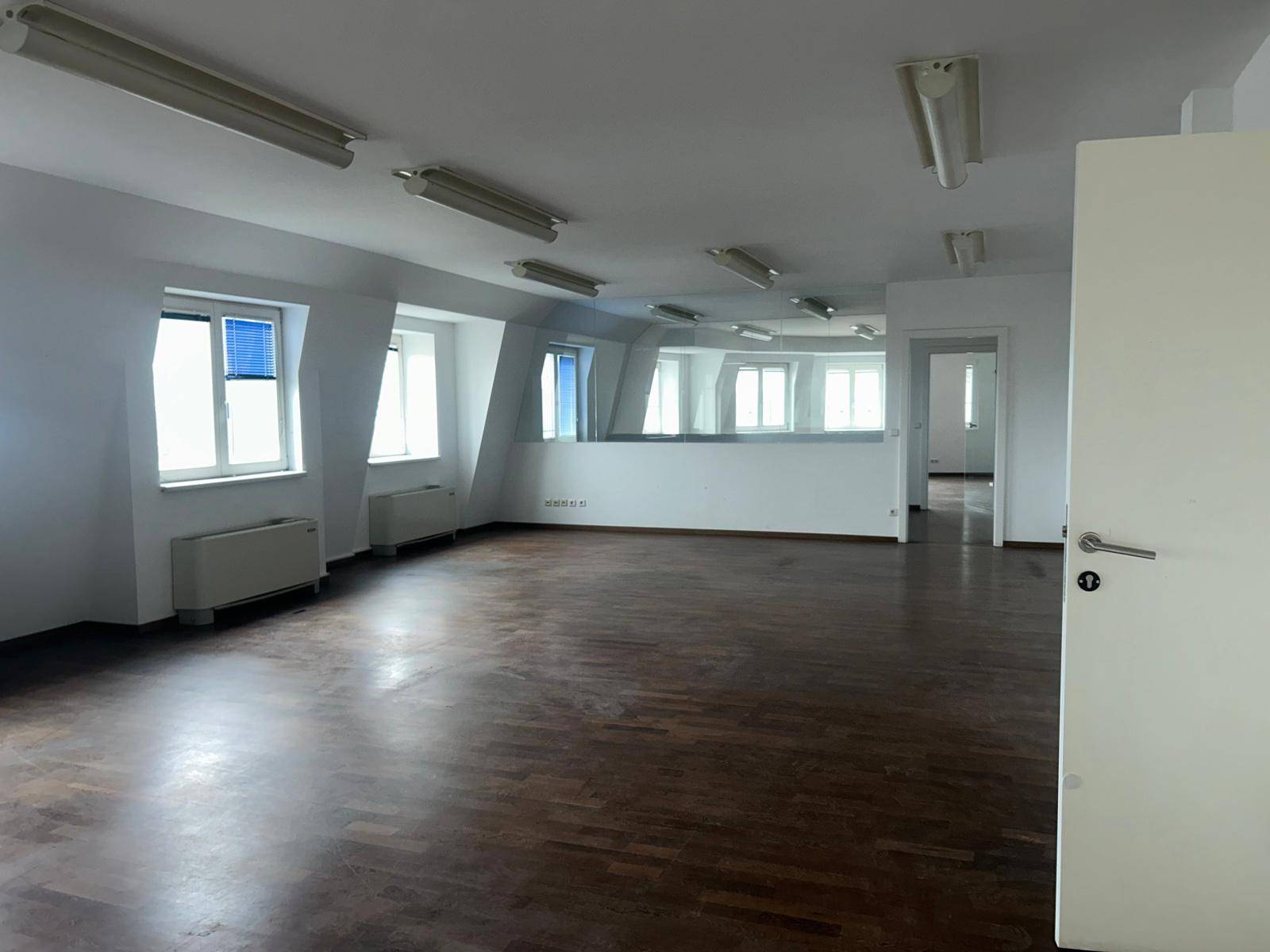 Großzügiger Bürobereich mit vielen Fenstern, Holzboden und moderner Beleuchtung, ideal für offene Konzepte.