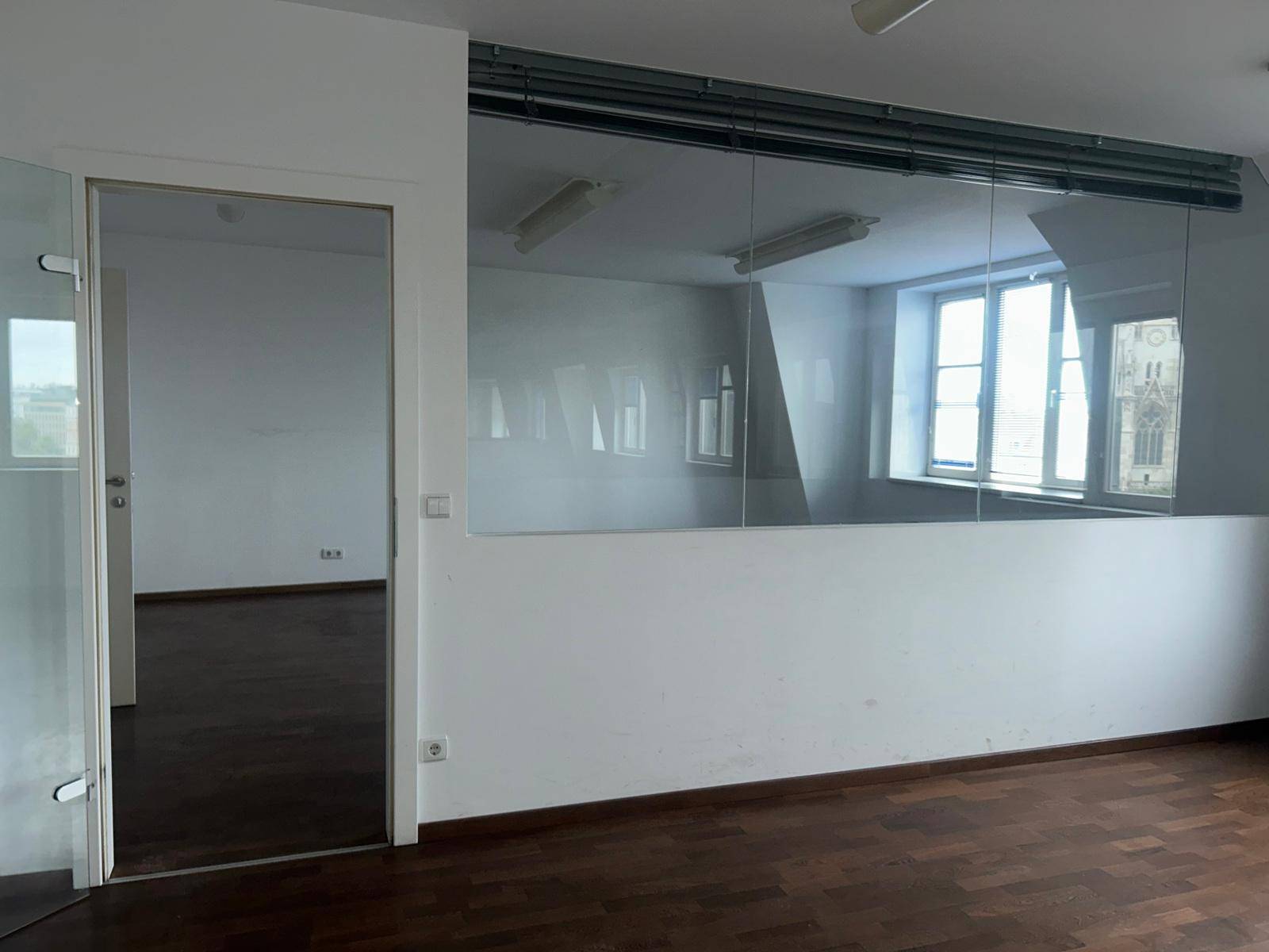Moderner Büroraum mit Glaswänden und dunklem Holzboden, der Offenheit schafft und viel Licht bietet.
