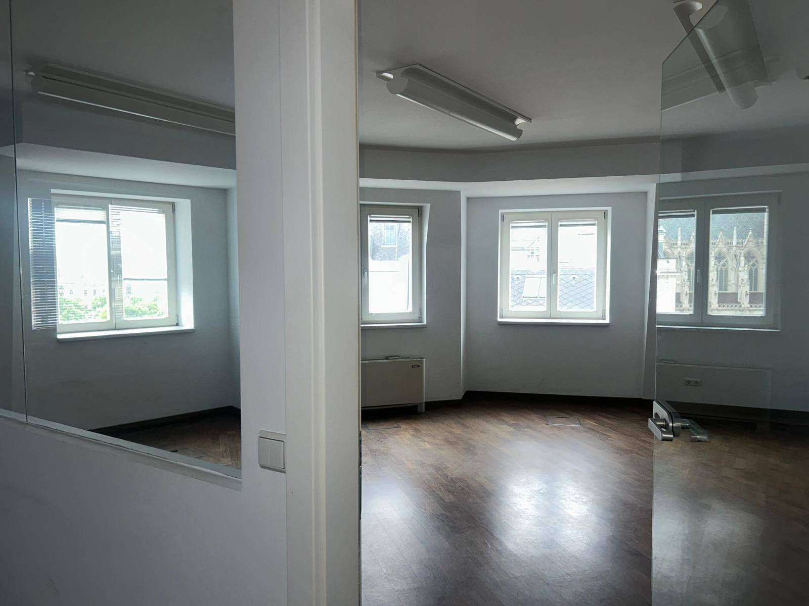 Heller Büroraum mit Holzboden und Fenstern, die einen Blick auf die Stadt ermöglichen.