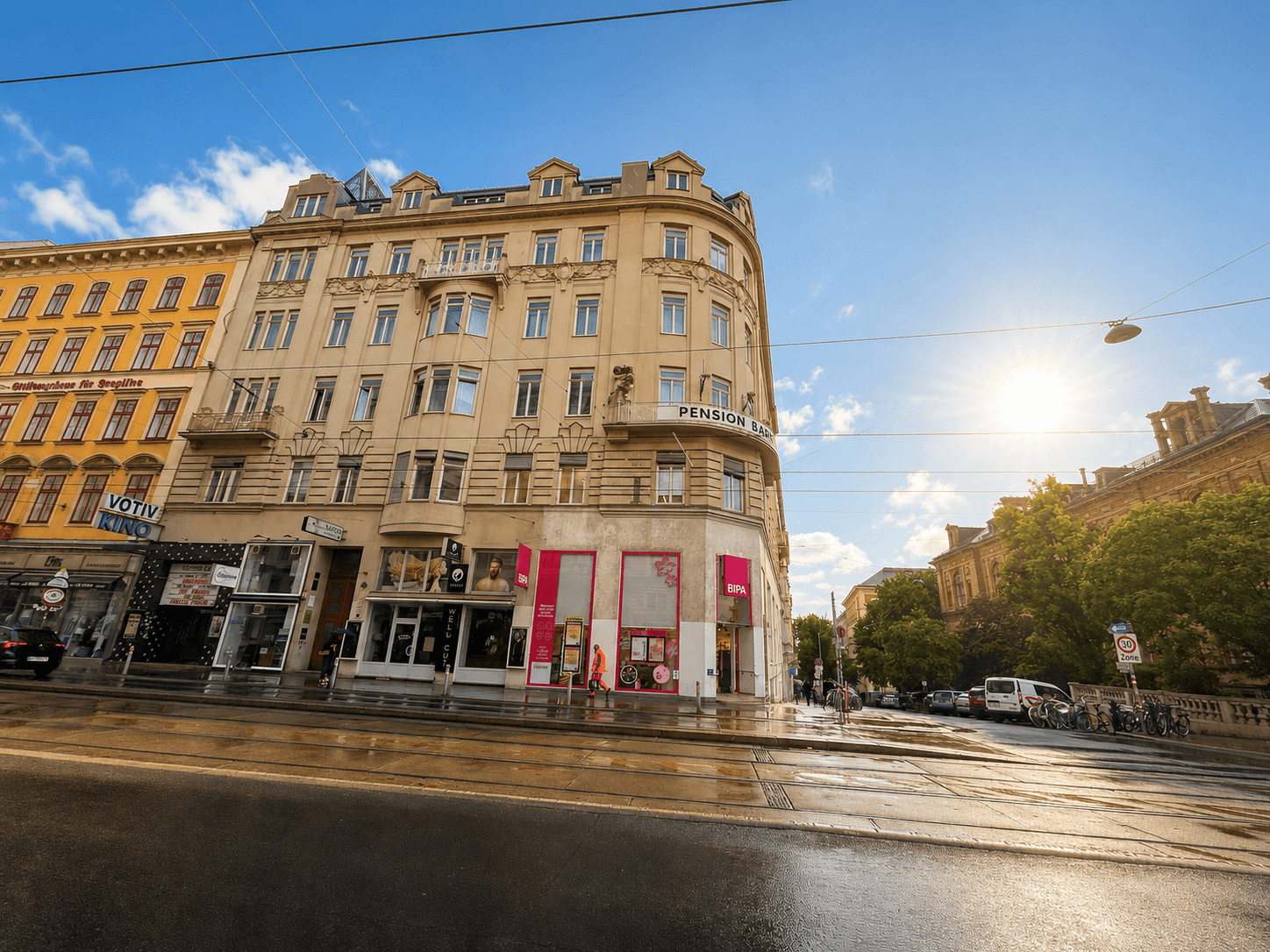 Historisches Gebäude an einer belebten Straße mit Geschäften und Sonnenschein, typisch für die Stadt.