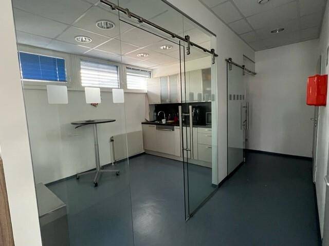 Kleine Küchenzeile hinter einer Glasschiebetür, ausgestattet für Pausen im Büro.