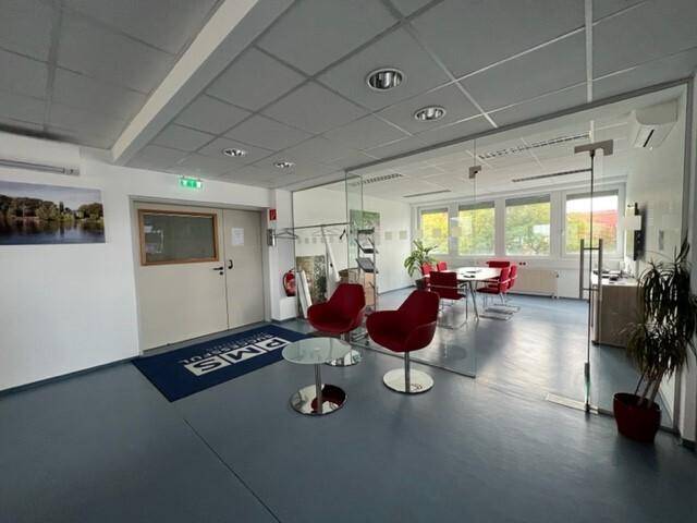 Offener Bürobereich mit Empfang und Blick auf einen Besprechungsraum mit roten Stühlen.