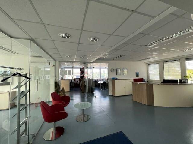 Großes, offenes Büro mit Empfangsbereich, Glaswänden und modernen roten Stühlen.
