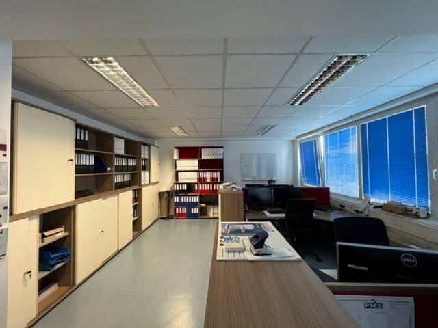 Großes Büro mit mehreren Arbeitsplätzen, umfangreichen Aktenschränken und blauen Jalousien.