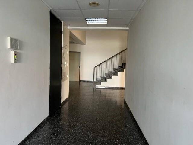 Langer Flur mit dunklem Terrazzoboden und einer Treppe, die in die oberen Stockwerke führt.