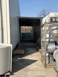 Überdachter Gang zwischen Gebäuden mit Lagergut und industrieller Ausstattung im Freien.