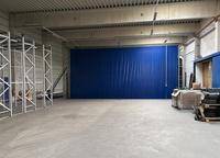 Geräumige Lagerhalle mit hohen Decken, Betonboden und einer großen blauen Trennwand.